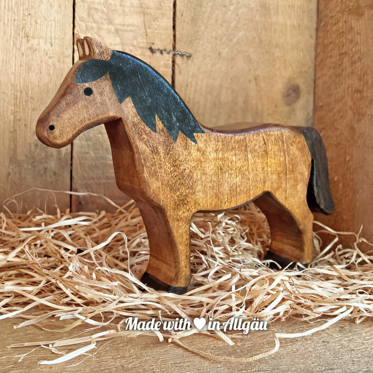 Handgefertigtes Holzspielzeug Pferd Haflinger Stute von Allgäuer Holztiere, stehend auf Holzspänen im Hintergrund raues Holz, aus bayerischem Ahornholz gefertigt, mit pflanzlichen Farben braun und schwarz bemalt, im Allgäu produziert und für Kinder ab 3 Jahren geeignet.