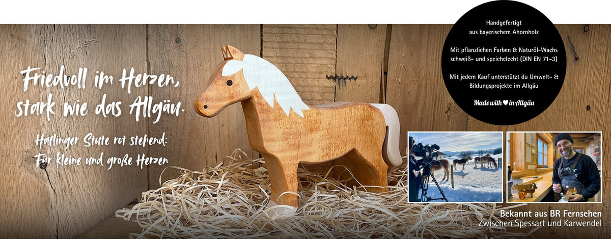 Handgefertigte Holzfigur einer Haflinger-Stute aus Ahornholz mit heller Mähne, stehend auf Holzwolle vor rustikalem Holz-Hintergrund. Links „Friedvoll im Herzen, stark wie das Allgäu. Haflinger Stute rot stehend: Für kleine und große Herzen“. Ein Hinweis zu Material, Verarbeitung und Unterstützung von Umwelt- und Bildungsprojekten im Allgäu. Unten rechts zwei Fotos (Haflinger im Winter, Daniel Köpf in der Werkstatt) mit Hinweis „Bekannt aus BR Fernsehen – Zwischen Spessart und Karwendel“